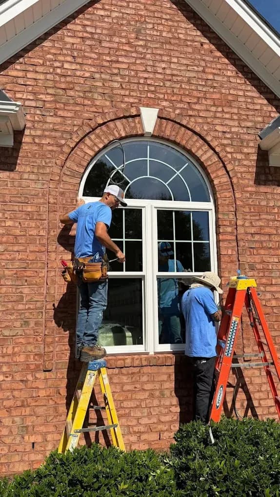 Clemmons workers installing custom rounded window on brick house