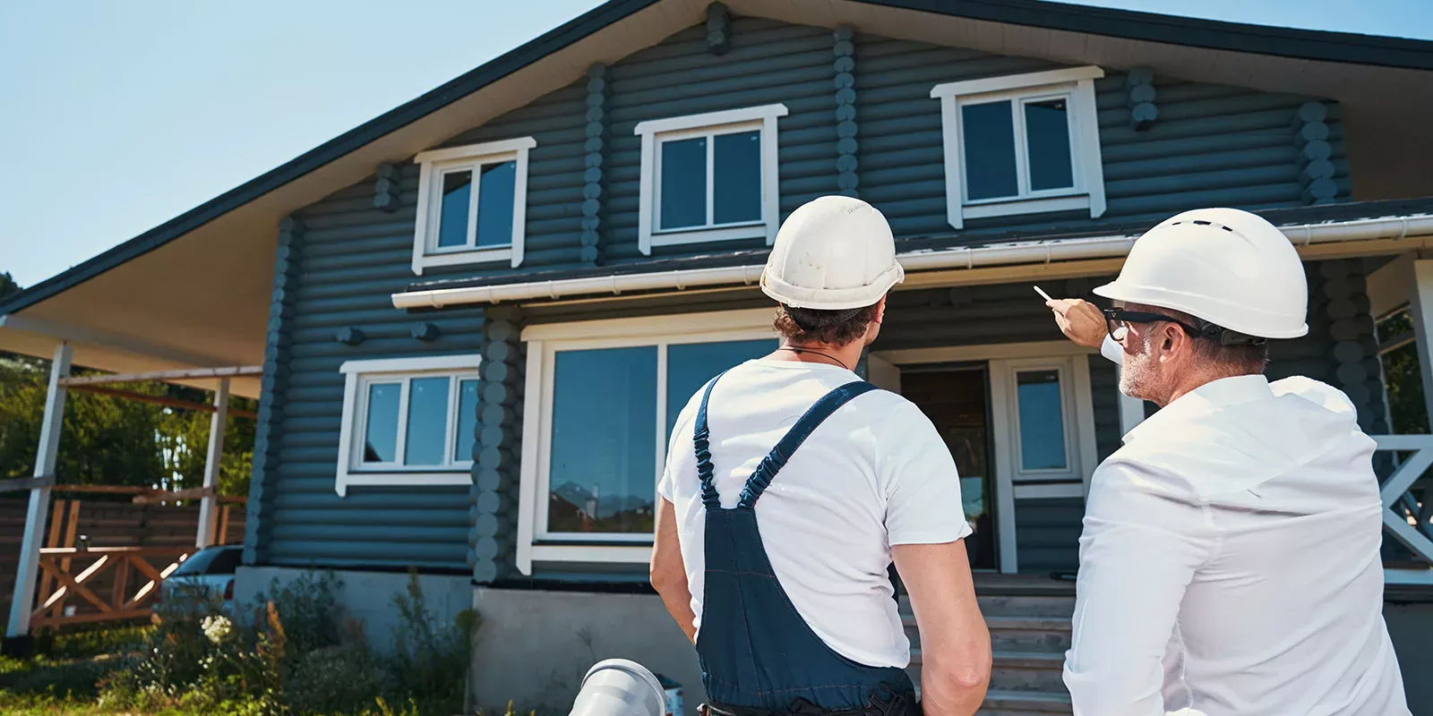 Two contractors looking at a home with grey wood siding