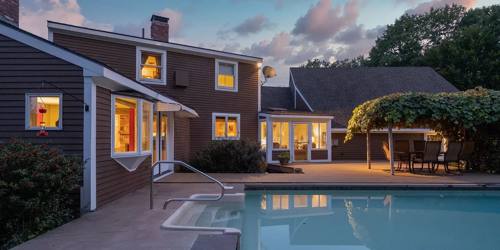 Outdoor view of grey house with lights on and pool